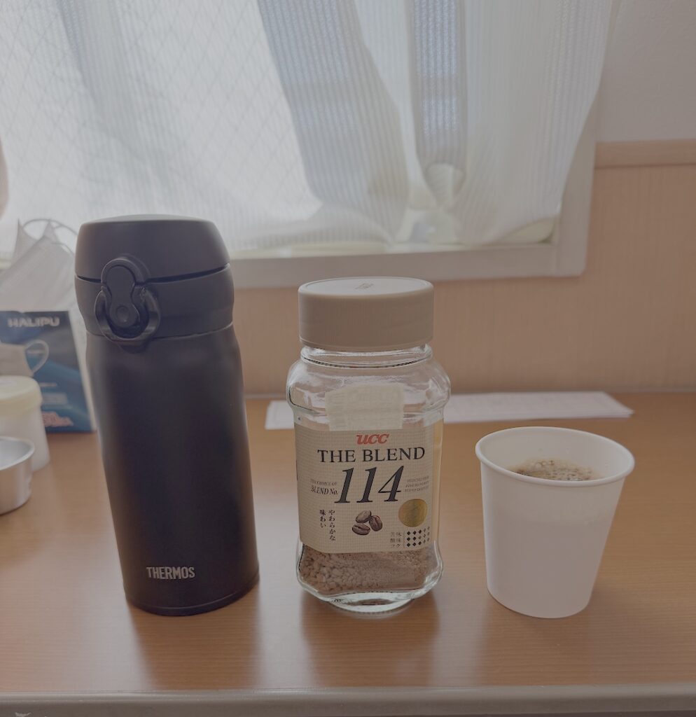 リハビリ病棟のテーブルに置かれたサーモスのボトルとインスタントコーヒー、紙コップのコーヒー