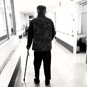 回復期病棟の廊下で杖を使って歩行訓練を行う後ろ姿