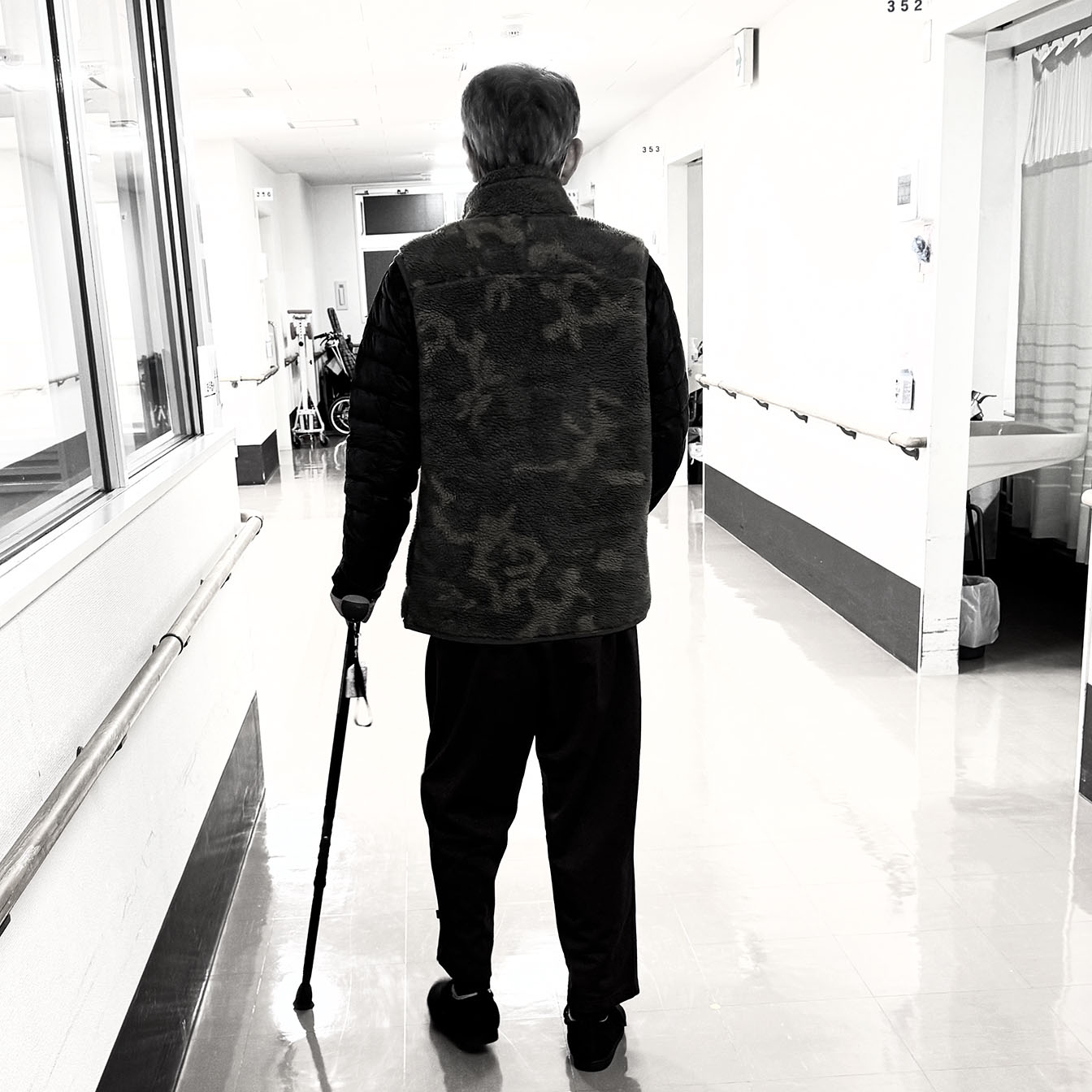 回復期病棟の廊下で杖を使って歩行訓練を行う後ろ姿