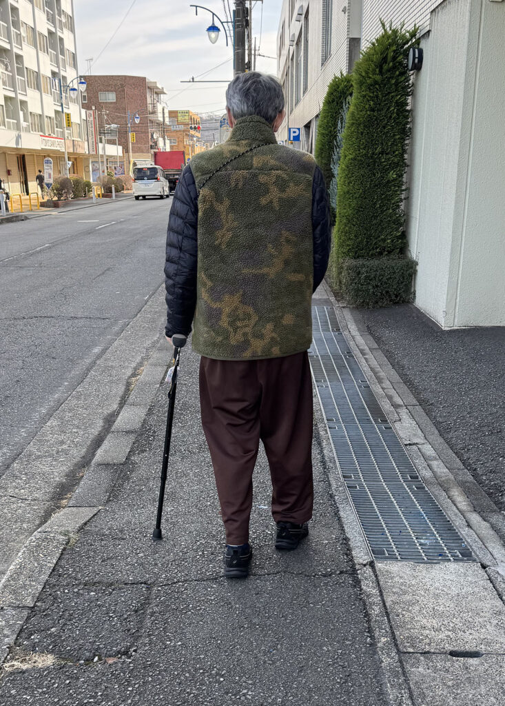 杖を使い、理学療法士とともに病院の外の歩道を歩く脳梗塞リハビリ中の様子